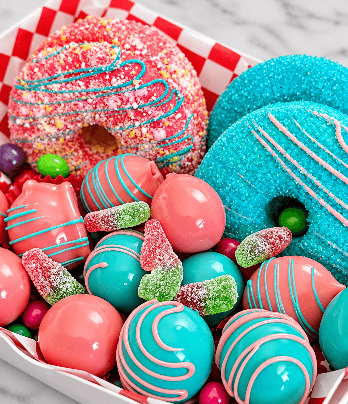 Vibrant pink and blue donuts, glossy truffles, and sour gummy candies in a checkered box.