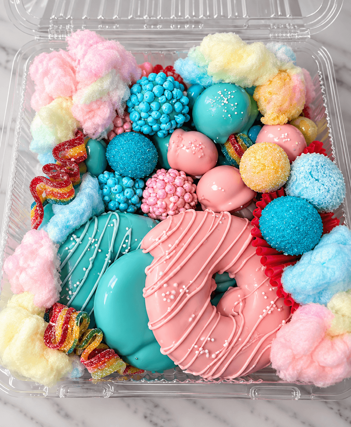 Pastel pink and teal glazed donuts surrounded by cotton candy and assorted colorful candy treats.